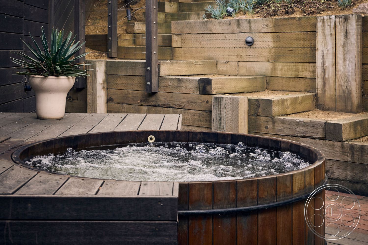 MCM 26 - surrounding greenery, exposed wood beams, outdoor relaxation area, natural landscape setting, wood deck flooring, concrete patio border, modern outdoor living space, wooden retaining wall, wood hot tub, curved hillside steps, potted agave plant, rustic wooden steps