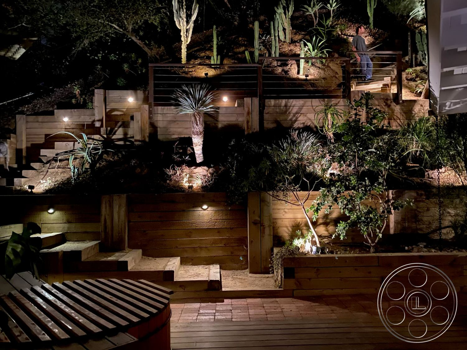 MCM 26 - outdoor seating area, landscaped hillside, eco-friendly landscaping, modern outdoor design, rustic wooden deck, exterior wooden steps, treated wood retaining walls, recessed outdoor lighting, spiral wooden stairs, desert plant landscaping, vertical wood fencing, natural wood planters, rock garden features, textured wood surfaces, ambient garden lighting, wooden handrail details, multi-level garden design, timber terrace, softscape and hardscape integration, hilltop retreat setting