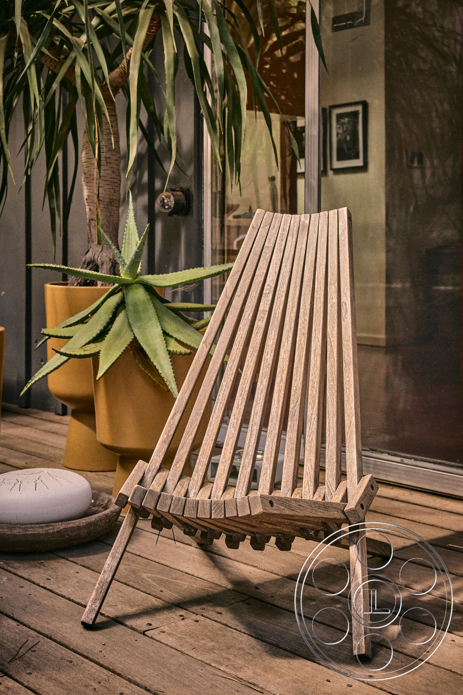 MCM 26 - relaxed seating, warm color palette, outdoor furniture, eco-friendly materials, natural wood finish, potted palm plant, glass sliding door, open-air living area, contemporary outdoor setting, wooden patio chair, slatted wood design, minimalist style chair, floor deck surface, modern garden aesthetic, textured wood grain, sunlight shadow play, crafted wooden frame, interior-exterior transition, decorative stone bowl, tropical plants backdrop