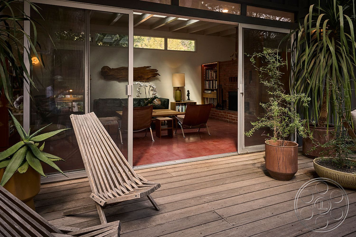 MCM 26 - minimalist design elements, textured wall finish, open-concept layout, decorative potted plants, earth-toned color palette, modern lounge chairs, wooden deck patio flooring, wood beam ceiling, contemporary outdoor seating area, exposed brick accent wall, functional outdoor living area, sliding glass patio doors, urban setting with greenery, indoor living space with natural light, interior living room with bookshelves