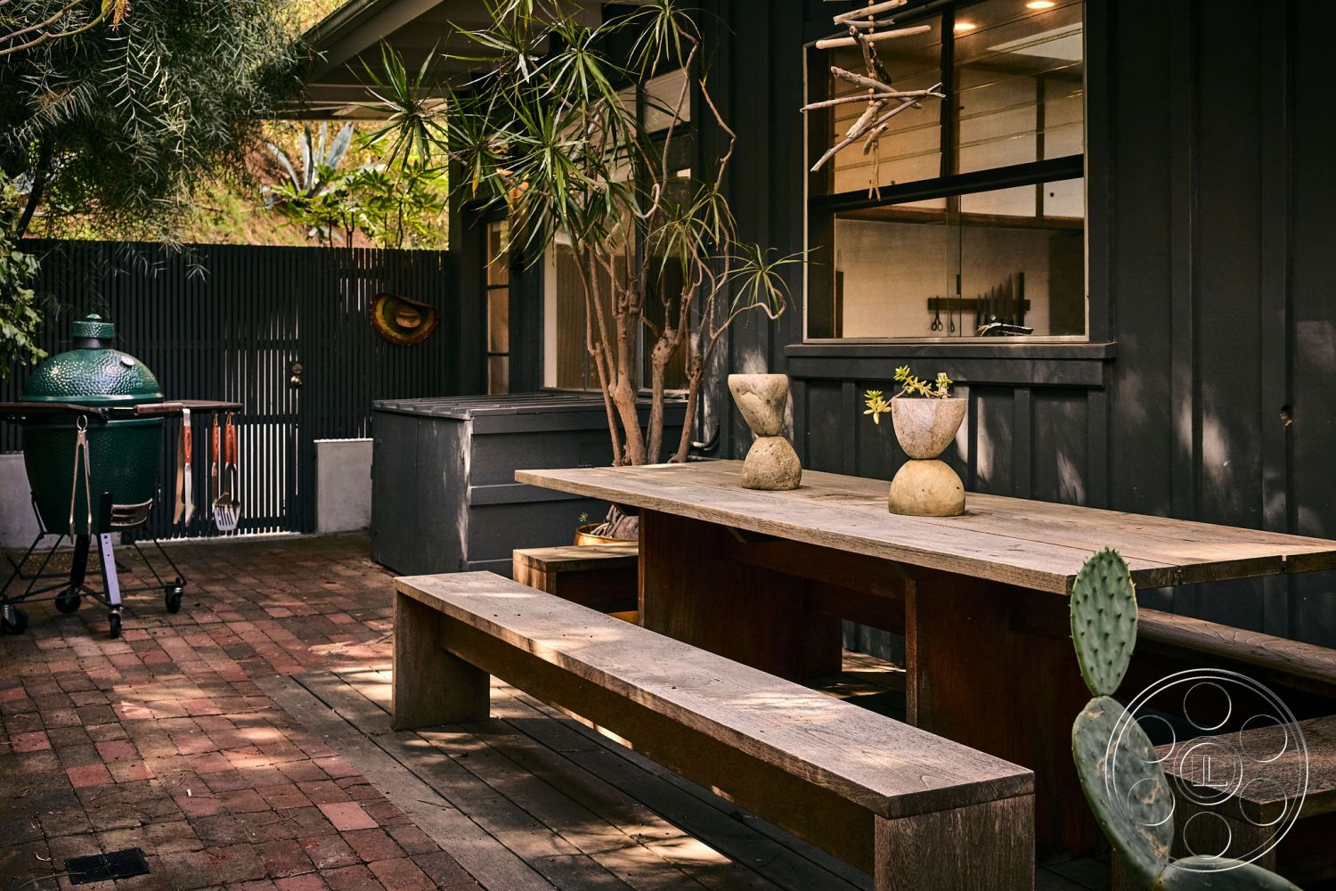 MCM 26 - exterior, natural wood furniture, contemporary outdoor space, neutral color scheme, modern outdoor seating, black wooden fence, concrete patio flooring, rustic outdoor decor, green ceramic grill, wooden patio dining table, brick paver patio base, landscaped tropical plants, low-profile planters, textured wood wall accents, casual outdoor dining area, vegetation accenting outdoor environment, dual-purpose garden, secluded backyard setting