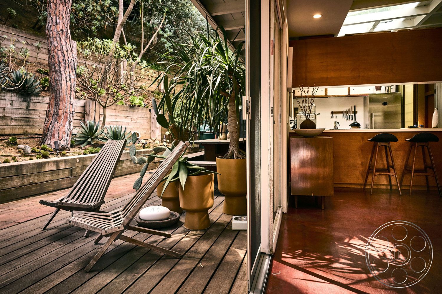 MCM 26 - large glass sliding doors, kitchen with stainless steel appliances, landscaped garden setting, wood beam ceiling, exterior wood deck flooring, open concept living area, natural light from skylights, urban garden patio, interior wooden cabinetry, concrete planter boxes, minimalist home design, red clay tile flooring, modern wooden lounge chairs, tropical plants and succulents, rustic wooden feature wall