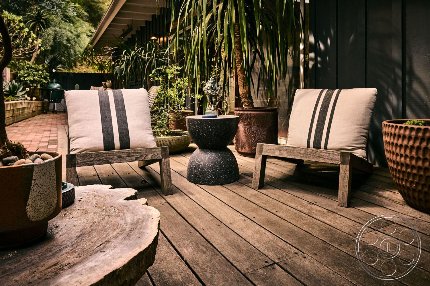 MCM 26 - large potted plants, textured fabric cushions, landscaped garden setting, wooden deck flooring, exterior patio area, contemporary outdoor chairs, round concrete side table, rustic log accent table, horizontal wooden slat walls, decorative terracotta pots