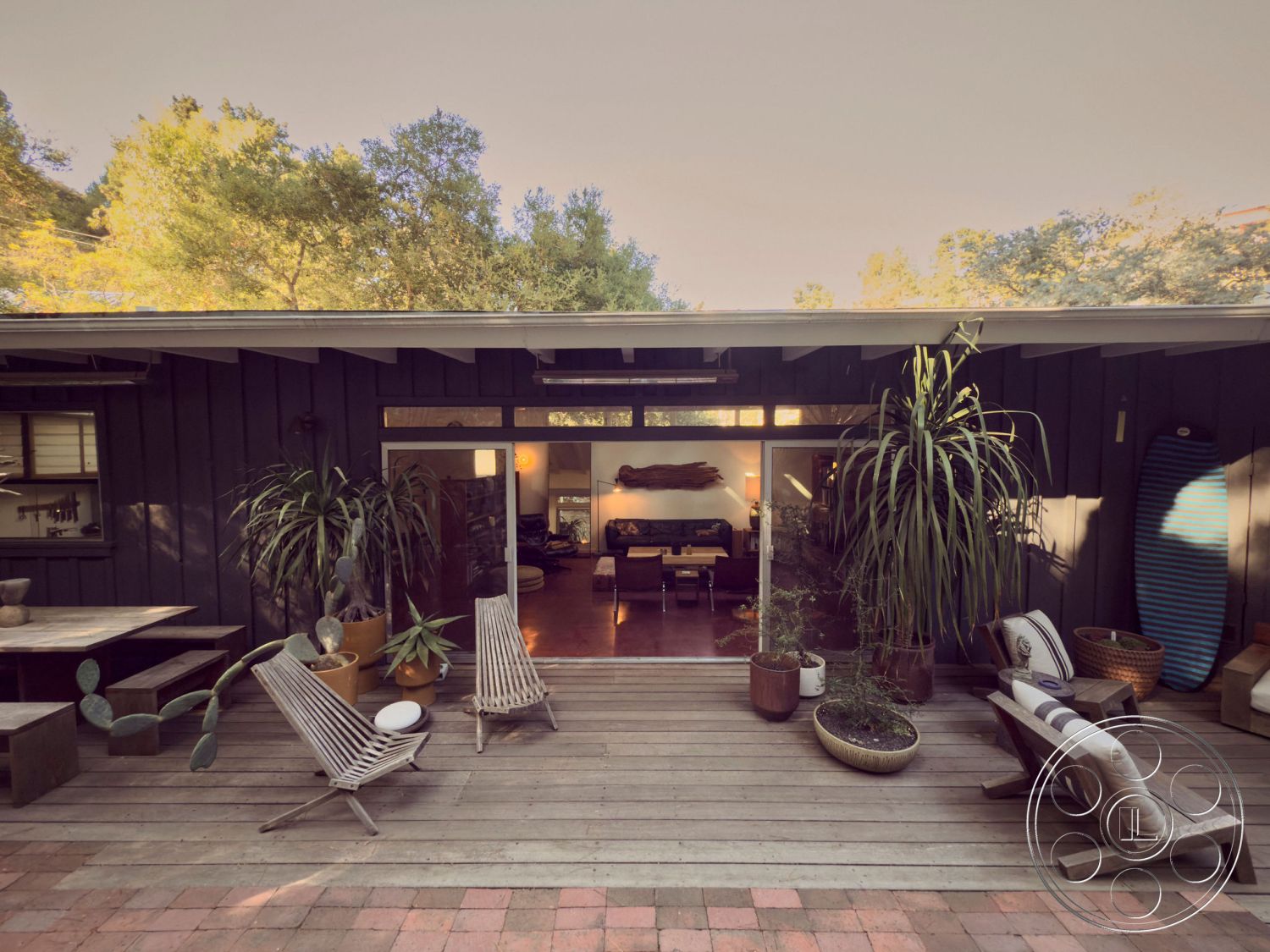 MCM 26 - modern outdoor furniture, natural light from large windows, wooden lounge chairs, exterior paver patio, interior contemporary decor, interior ambient lighting, exterior wooden deck, interior textured wall art, interior open living space, plant accent decor, interior modern living room, urban home setting, exterior plank deck flooring, inside glass sliding doors, exterior landscape greenery, spacious patio area