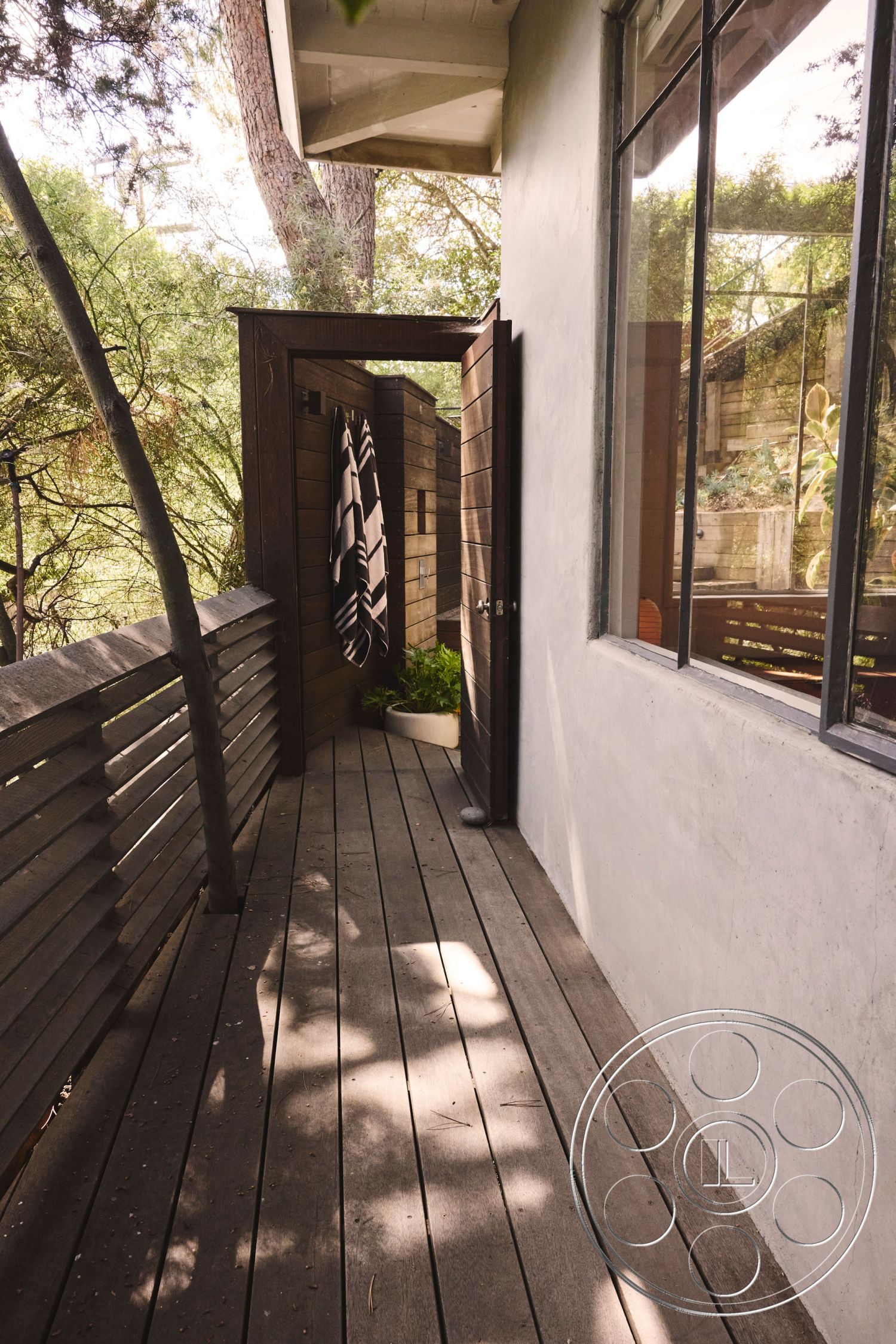 MCM 26 - sliding glass door, vaulted ceiling, open outdoor space, modern home, environmentally integrated design, natural landscape view, textured plaster wall, exterior wood deck, exterior stone pathway, minimalist architectural style, wood railing details, concrete wall treatment, wooden outdoor storage, fenced wooded area, sun-drenched deck