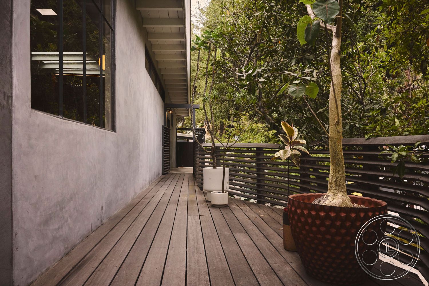 MCM 26 - large glass windows, surrounding greenery, natural landscape view, exterior stucco walls, minimalist architectural style, slatted wood railing, wood plank decking, contemporary outdoor setting, rectangular planter pots, open outdoor walkway