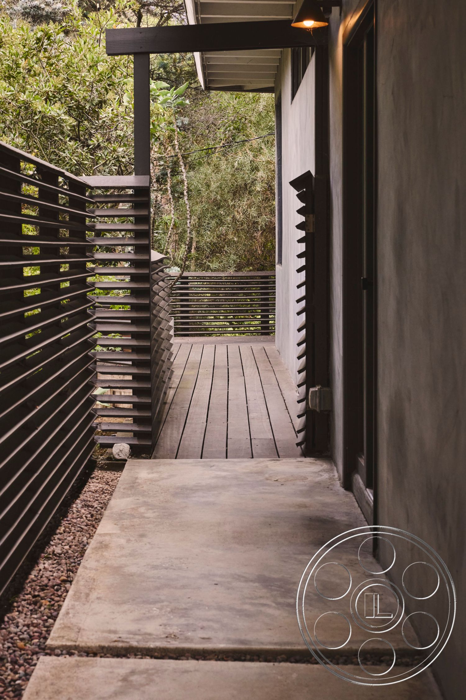 MCM 26 - sustainable design features, smooth concrete finish, natural landscape view, rustic garden setting, modern minimalist architecture, exterior concrete pathway, wood deck walkway, horizontal wood slat fencing, textured wood railings, concrete slab surface, weathered wood elements, private outdoor corridor