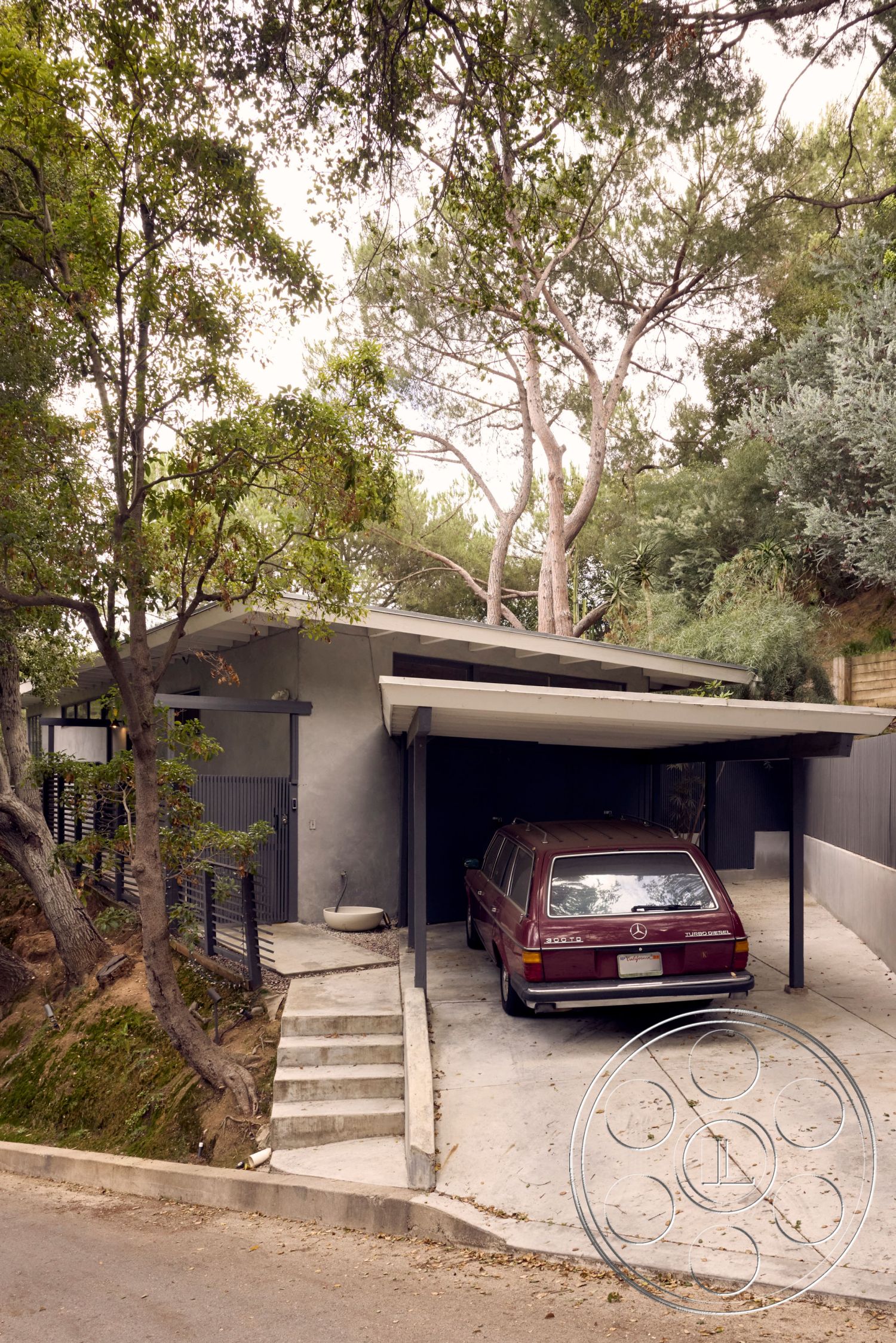 MCM 26 - exterior concrete driveway, interior open-concept living space, exterior hillside location, exterior concrete steps, exterior metal railing, exterior flat roof overhang, exterior wood accent paneling, exterior landscape with mature trees, exterior urban garage parking, exterior designed for natural light, exterior minimalist architecture, structural exposed roof beams, architectural contemporary style, setting suburban environment, surrounding natural greenery, constructed with durable materials, exterior smooth concrete walls