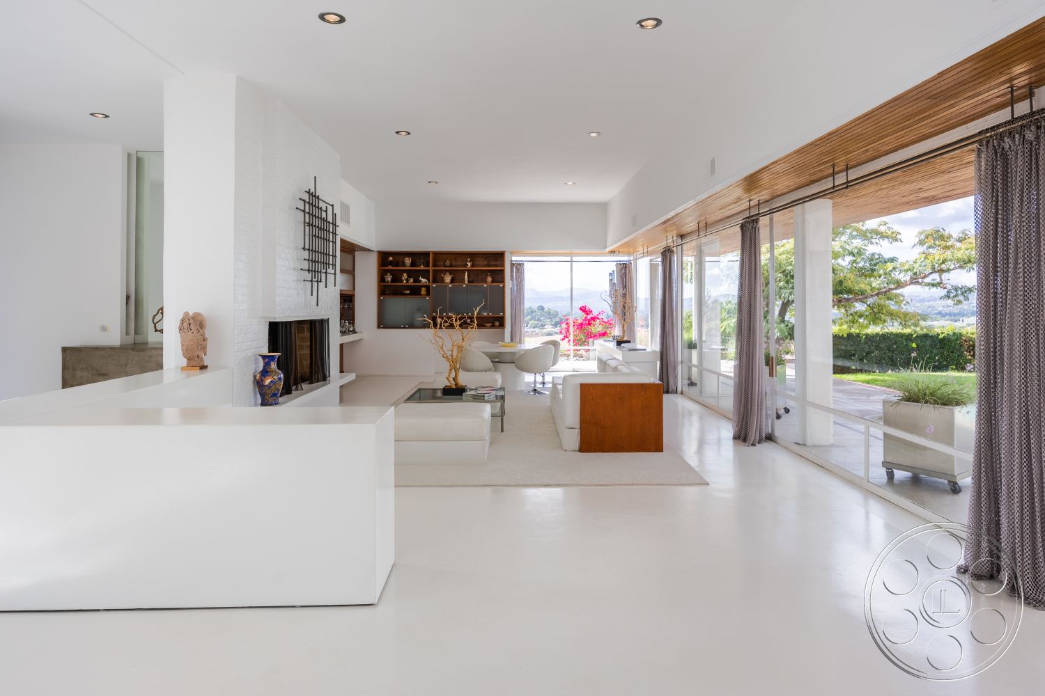 Sinatra House - interior textured wall treatment, interior muted color palette, interior floor-to-ceiling glass windows, interior open floor plan layout, interior decorative stone accents, interior wooden beam ceiling, interior seamless indoor-outdoor flow, interior white polished concrete floors, interior white brick fireplace surround, interior contemporary minimalist furniture, interior light gray area rug, interior natural light from sliding glass doors, interior sculptural decor elements, interior modern art display, interior multi-functional living space, interior built-in shelving units, interior luxury living area