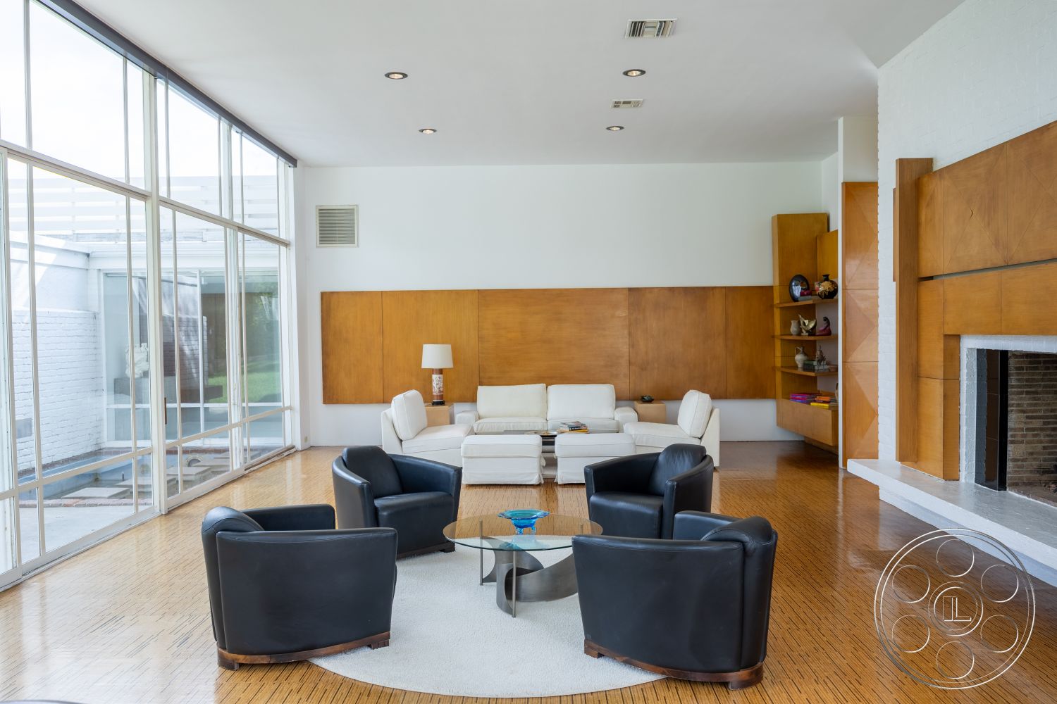 Sinatra House - neutral color palette, indoor-outdoor flow, urban setting, exposed brick fireplace, soft area rug, contemporary lighting fixtures, round glass coffee table, open floor plan layout, built-in wooden shelves, polished hardwood flooring, textured wallpaper accent, exposed wood paneling wall, glass wall with natural light, white leather sectional sofa, black leather armchairs, minimalist fireplace surround, mid-century modern interior