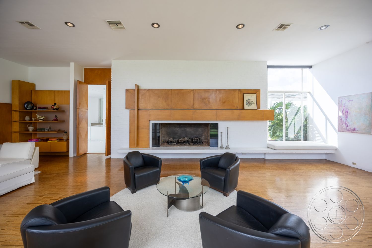 Sinatra House - neutral color palette, natural light, hardwood flooring, clean lines, open floor plan, seating area, geometric shapes, wood accent wall, mid-century modern style, round glass coffee table, modern minimalist design, interior living room, exposed brick fireplace wall, built-in wooden shelves, flush mount ceiling lights, contemporary art display, glass window wall, black leather armchairs, indoor plants view