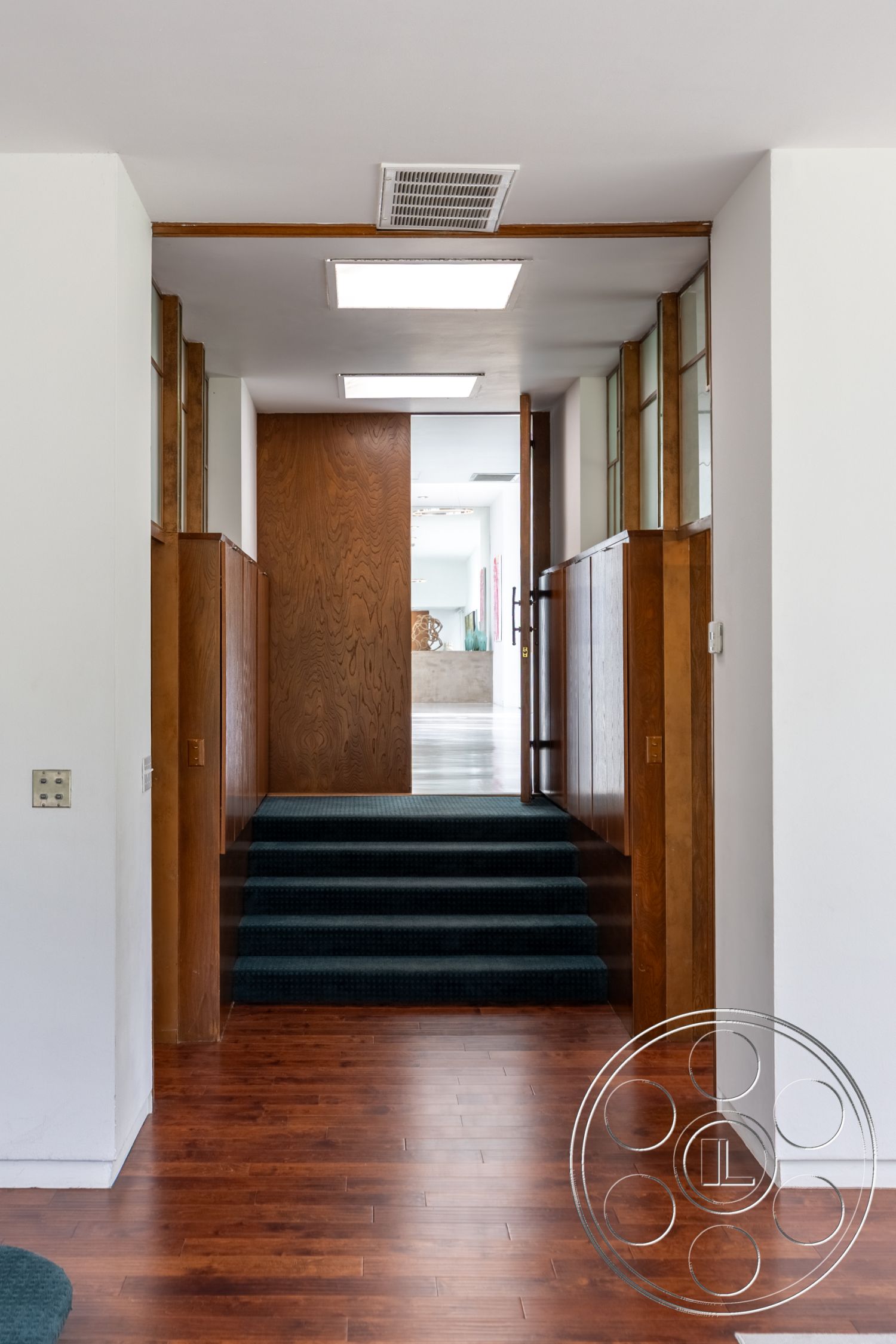 Sinatra House - earthy color palette, modern architectural style, interior recessed lighting, interior hardwood floor, interior open floor plan, interior wood paneling details, interior carpeted staircase, interior vaulted ceilings, exposed wood grain surfaces, walkway with wooden doors, interior white wall finishes, mid-century modern features, glass partition elements