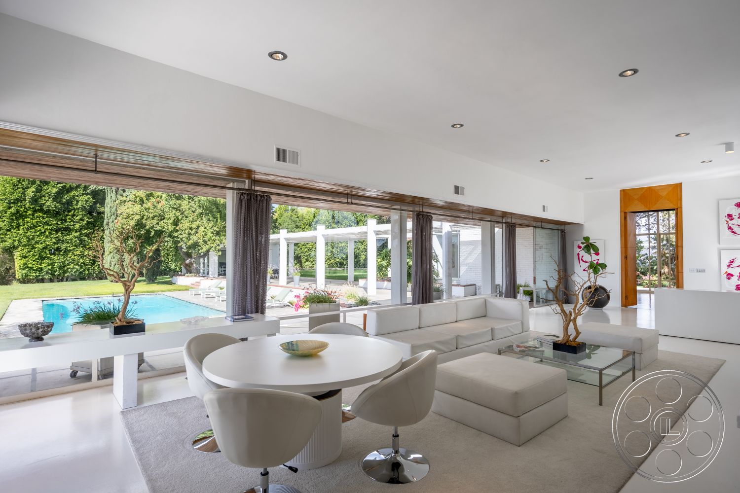 Sinatra House - polished concrete flooring, open concept layout, upholstered dining chairs, floor-to-ceiling windows, city skyline view, contemporary art on walls, outdoor pool area, modern round dining table, white painted walls, minimalist furniture design, light and airy ambiance, landscaped garden patio, wood beam ceiling accents, interior modern living room, rectangular glass coffee table, curtains for natural light control, chef's kitchen with white cabinetry, glass sliding doors to patio, natural lighting throughout, sun-drenched space with greenery