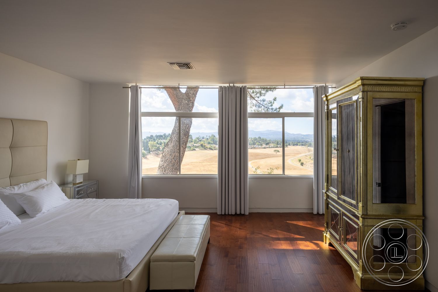 Sinatra House - interior neutral color palette, interior hardwood bedroom floors, interior cozy atmosphere, interior floor-to-ceiling windows, interior white painted walls, interior minimalist design, interior modern upholstered bed, interior mountain view, interior contemporary style, interior gold accent cabinet, interior sheer window treatments, interior bedside lamp, interior bench seat at foot of bed