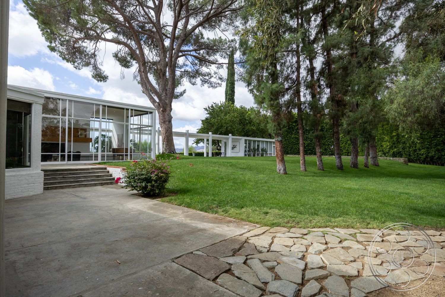 Sinatra House - exterior concrete driveway, exterior wood deck, exterior sliding glass doors, exterior landscaped garden, exterior modern architectural style, exterior stone pathway, exterior glass walls, exterior green lawn setting, exterior tall pine trees, exterior brick border, exterior steps leading to house, exterior clean lines and forms