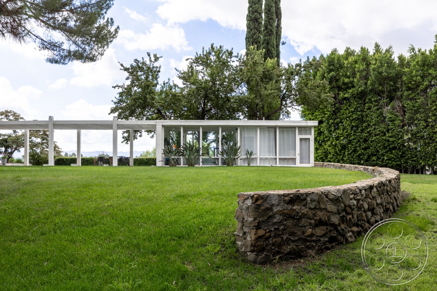 Sinatra House - exterior, open floor plan, glass walls, seamless indoor-outdoor transition, steel framing, city skyline view, modern outdoor space, flat roof design, rectangular patio area, minimalist architectural style, surrounded by mature trees, green lawn setting, stone landscape wall, concrete posts, soft landscaping features