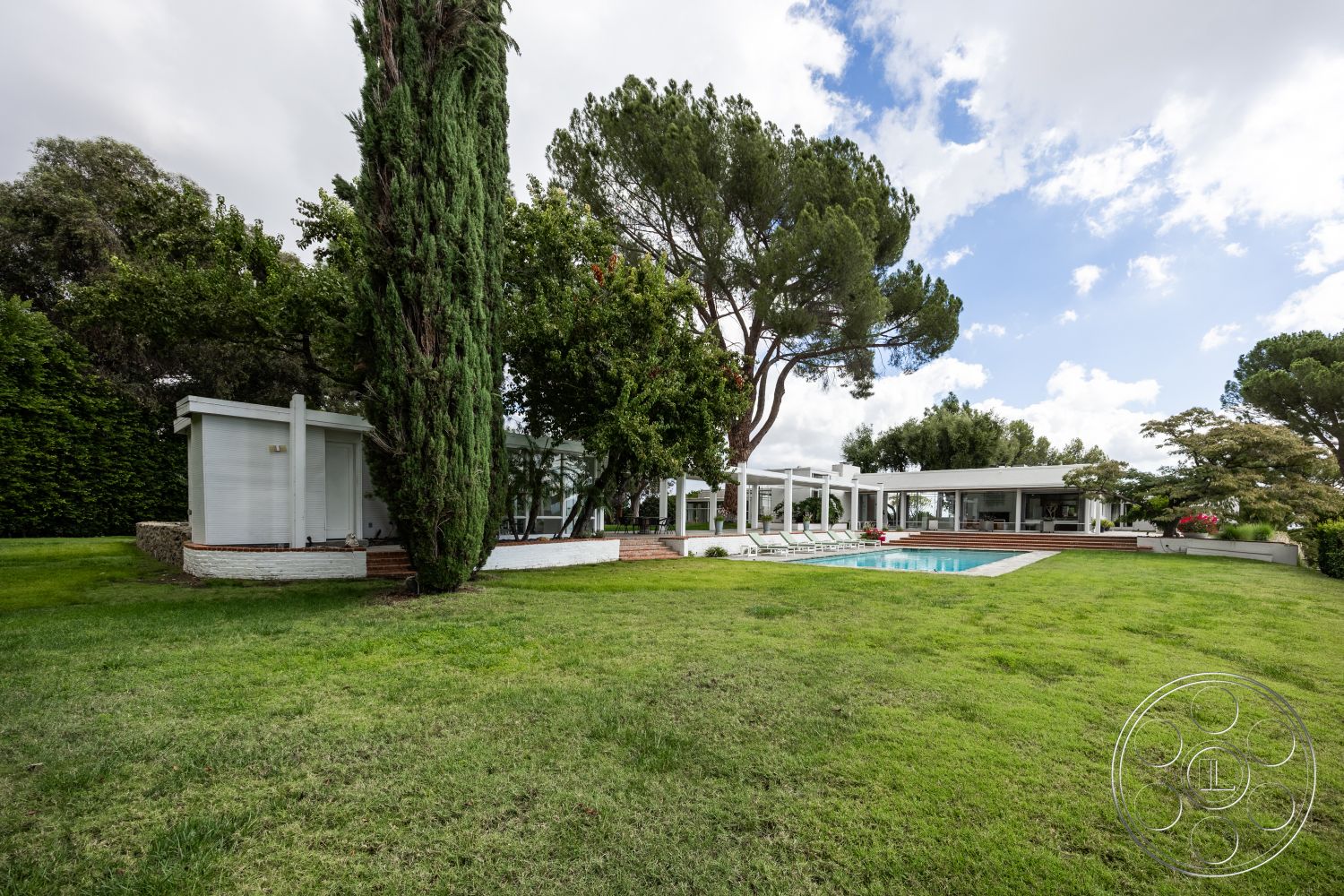 Sinatra House - large windows, exterior, landscaped garden, white stucco walls, modern architecture, flat roof, minimalist design, glass sliding doors, wooden deck, surrounding greenery, exposed wooden beams, rectangular swimming pool, grass lawn, single-story home, outdoor lounge area, concrete pool border, stone patio area, cedar trees in landscape