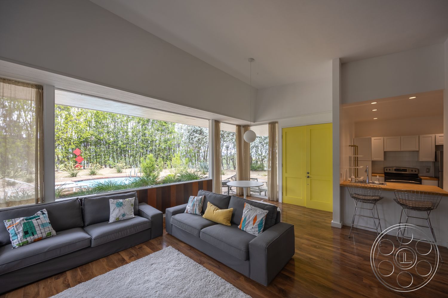 Sinatra House - minimalist design elements, glass sliding doors, outdoor seating area, framed artwork, floor-to-ceiling windows, soft area rug, hardwood living room floors, neutral color palette walls, contemporary open-plan layout, modern kitchen with stainless steel appliances, yellow double doors, textile accent pillows, light fixture pendant, exterior view of landscaped backyard, interior with high ceilings, wire bar stools, potted greenery indoors, open space between living and dining areas