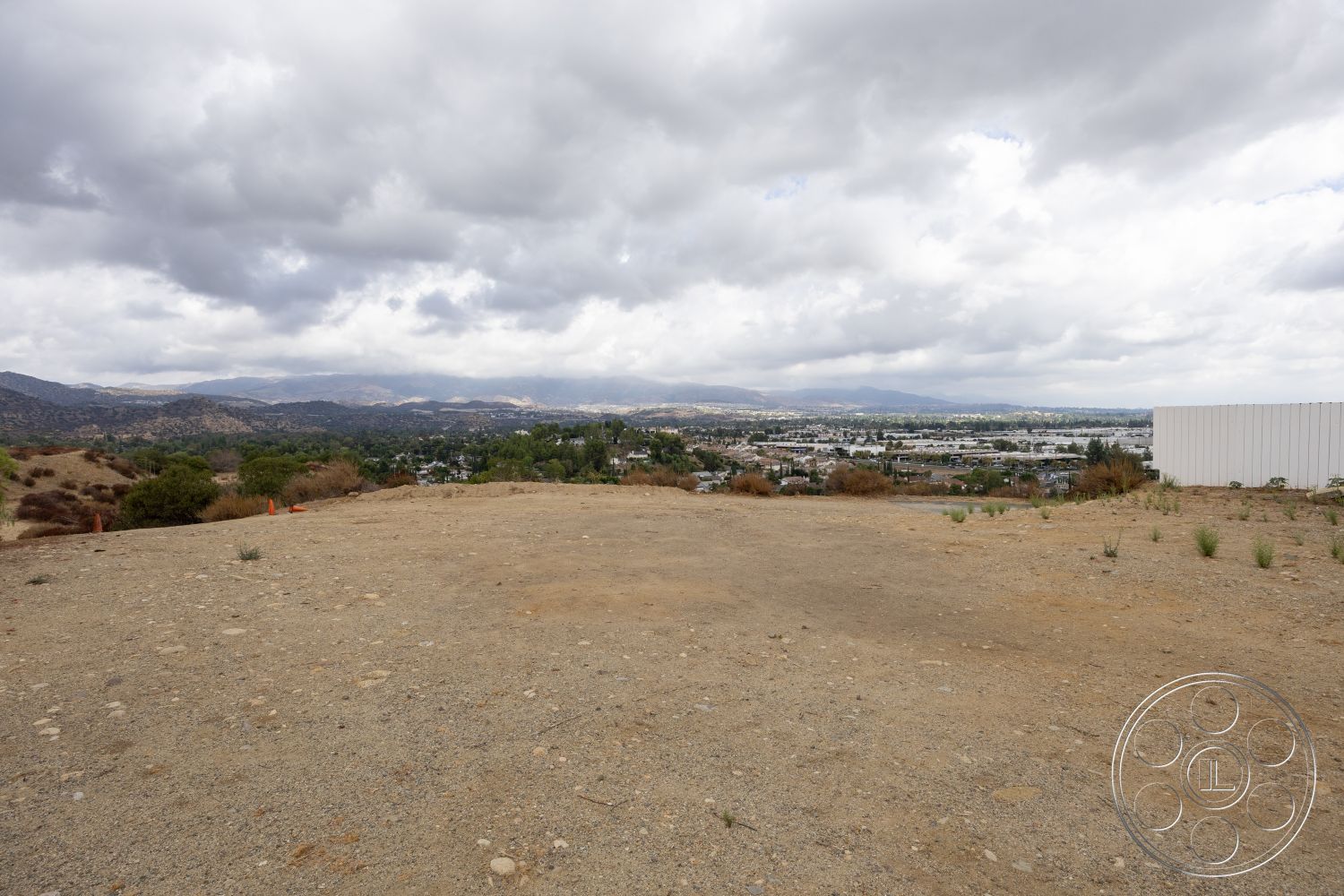 Sinatra House - city skyline view, rocky terrain, suburban environment, hillside location, open landscape, undeveloped land, cloudy sky, natural dirt ground surface, distant mountain range, gravelly soil base