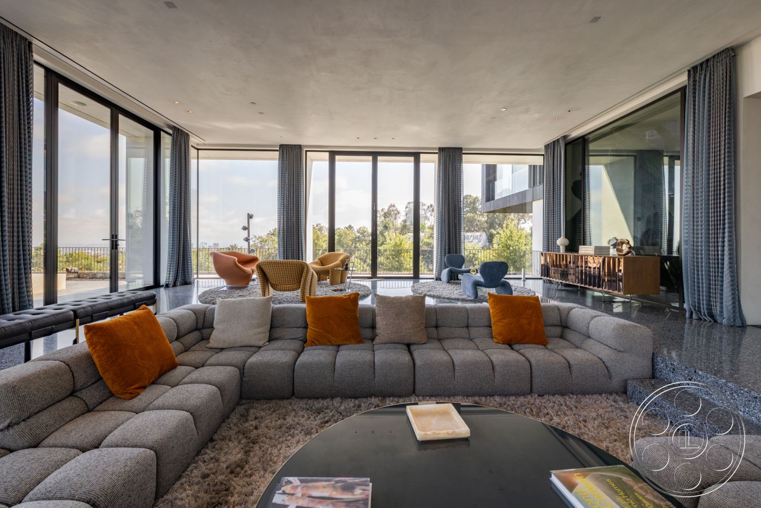 Modern 513 - polished concrete flooring, soft area rug, open concept living room, seamless indoor-outdoor flow, round marble coffee table, textured fabric curtains, urban hillside location, floor-to-ceiling glass windows, geometric shapes in furniture design, minimalist architectural details, exposed concrete interior walls, modern sectional sofa with orange accents, integrated wooden media console, contemporary accent chairs, view of landscaped outdoor terrace, warm ambient lighting fixtures, gradient ceiling treatment, luxury modern interior