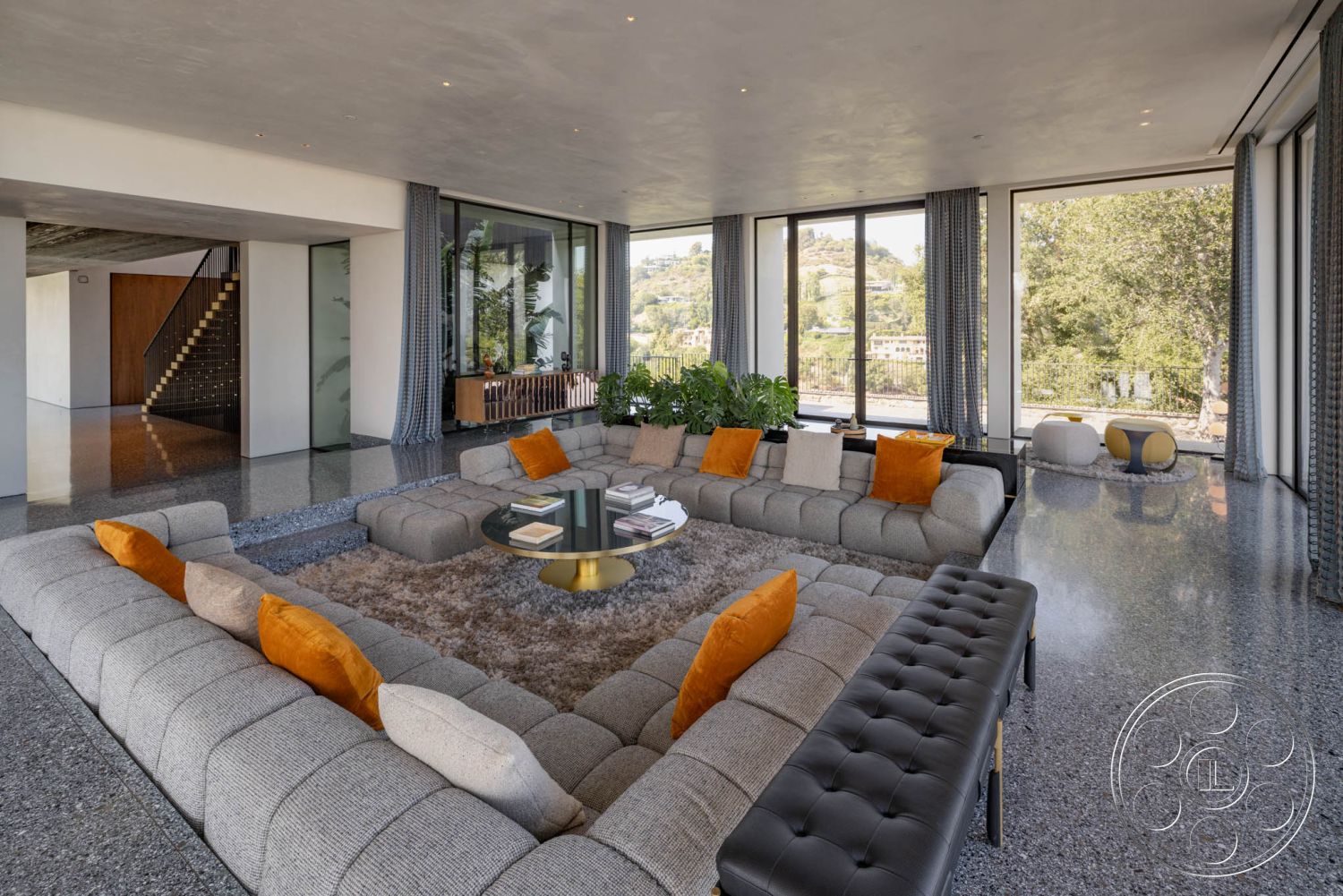 Modern 513 - neutral color palette interior, modern pendant lighting interior, exposed concrete walls interior, polished terrazzo flooring interior, open concept living space interior, rectangular sectional sofa with orange accents interior, floor-to-ceiling windows with mountain view interior, glass coffee table with books interior, integrated wood storage unit interior, textured ceiling with recessed lighting interior, soft area rug under coffee table interior, curved plant features interior, modern staircase with black metal railings interior, luxurious texture contrasts interior