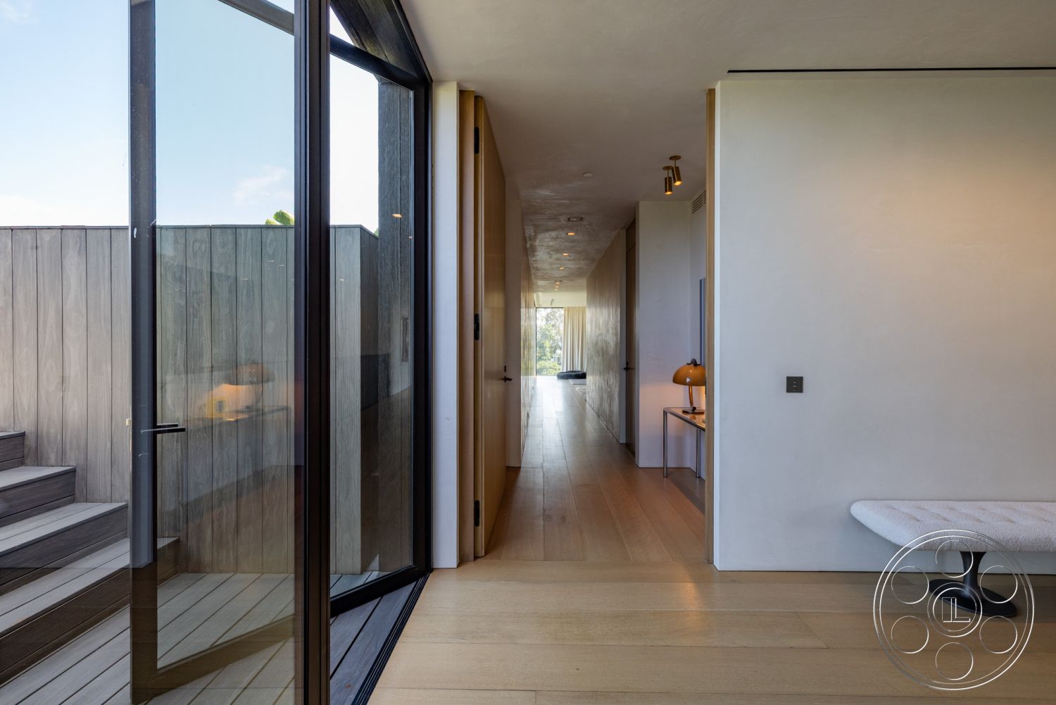 Modern 513 - neutral color palette, open-concept layout, natural light-filled space, interior floor-to-ceiling windows, exterior glass sliding doors, clean lines architecture, smooth plaster walls, architectural recessed lighting, interior wood plank flooring, modern minimalist design elements, exposed concrete wall details, dark wood paneling hallway, contemporary staircase with wooden steps, integrated built-in furniture design, minimalistic hallway decor, outdoor wooden deck access, single-story open corridor, sight lines to outdoor area, sliding glass door transitions, modern bench seating