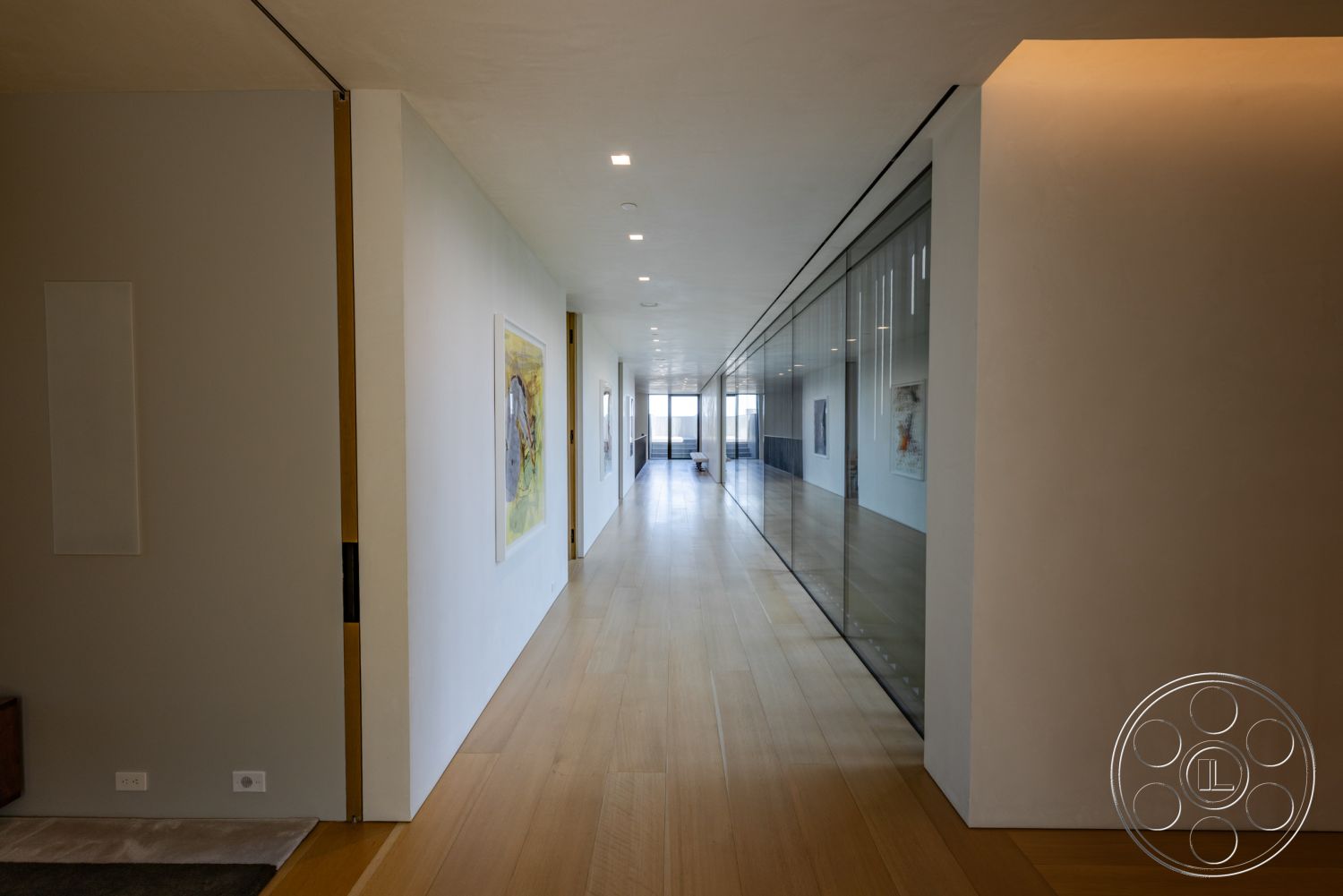 Modern 513 - neutral color palette, open concept layout, well-lit corridor, modern architectural style, spacious hallway, contemporary interior, minimalist interior design, smooth plaster walls, linear recessed lighting, artwork display on walls, natural light flooding interior, light hardwood hallway flooring, floor-to-ceiling glass partition wall, simple wood trim, seamless transition to living area, elevated views from corridor