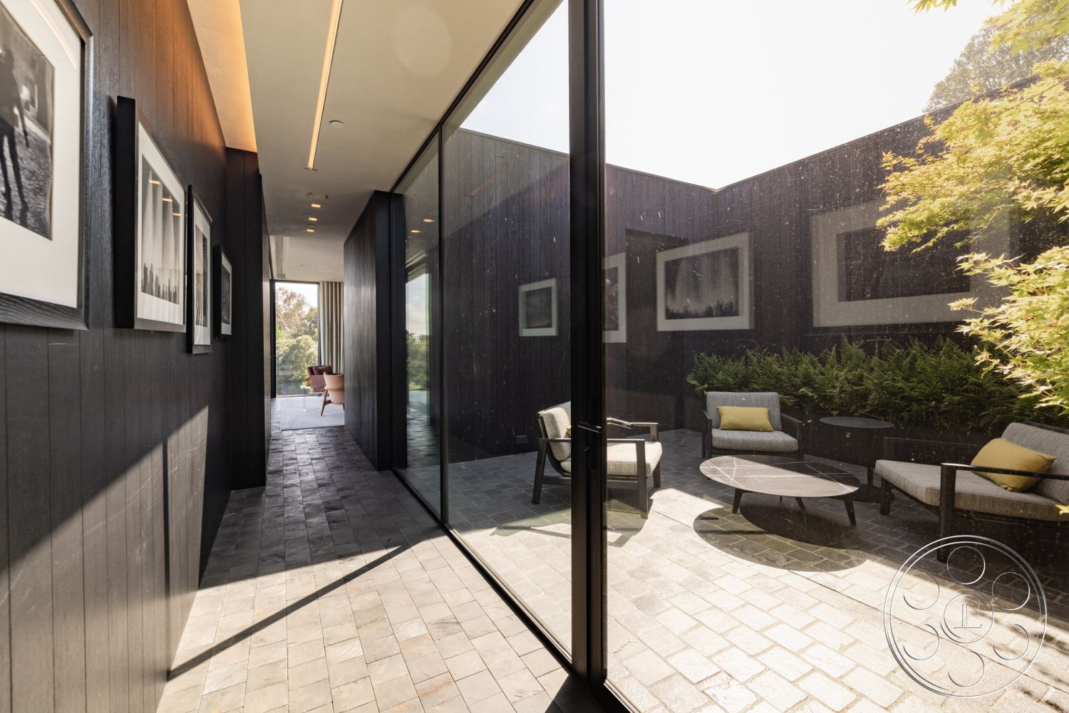 Modern 513 - neutral color palette, floor-to-ceiling windows, suburban backyard, contemporary seating area, modernist aesthetic, slate tile flooring, interior recessed lighting fixtures, minimalist architectural design, curved exterior walls, exterior glass wall, modern round coffee table, exterior paved patio flooring, large sliding glass door, interior black wood paneling, framed art wall decor, outdoor green landscaping, outdoor lounge chairs with cushions, open courtyard setting, tranquil outdoor space