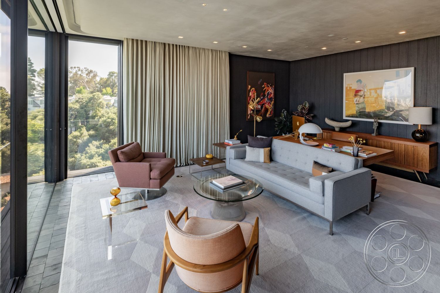 Modern 513 - textured plaster ceiling, decorative throw pillows, dark wood paneling wall, glass floor-to-ceiling windows, neutral color curtains, contemporary silver table lamp, minimalist gray sofa, modern round glass coffee table, soft cream area rug, wooden mid-century modern sideboard, blue and orange abstract art wall decoration, curved mid-century modern accent chair, stylish office desk setup, urban green view