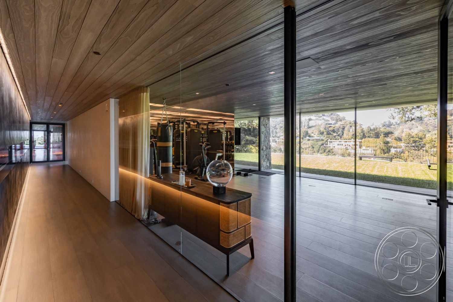 Modern 513 - neutral color palette, minimalist aesthetic, indoor-outdoor flow, stainless steel finishes, seamless transition to outdoor space, warm wood accents, contemporary architectural style, recessed lighting fixtures, interior hardwood flooring, open floor plan design, natural light from floor-to-ceiling windows, glass partition wall, smooth drywall finish, exposed wood ceiling planks, modern gym area, built-in cabinetry with lighting, landscaped yard view, functional workout space, elegant interior design