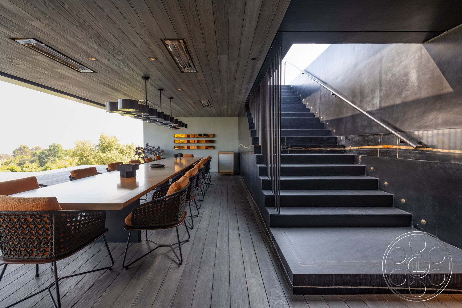 Modern 513 - exterior, open floor plan, modern workspace, floor-to-ceiling windows, horizontal wood accents, woven black chairs, natural landscape view, contemporary architectural style, minimalist interior design, glass partition wall, sculptural decor elements, dark wood ceiling panels, black concrete staircase, steel chandelier lighting, linear dining table, floating black concrete steps, outdoor dining setting