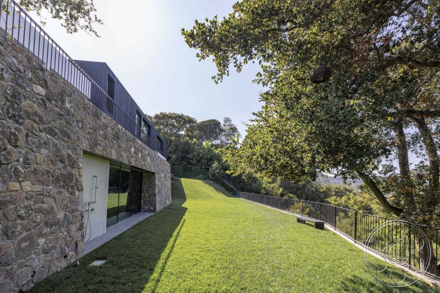 Modern 513 - open grassy area, contemporary architectural style, modern home design, natural light exposure, exterior glass sliding doors, metal railing balcony, exterior stone wall cladding, natural hillside setting, landscaped lawn area, minimalist patio space, deep overhanging roof eaves, urban contemporary exterior, suburban backyard environment