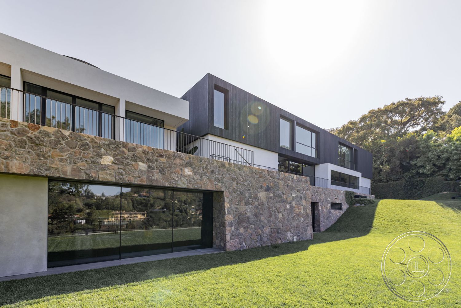 Modern 513 - suburban setting, flat roof design, contemporary architectural style, interior open floor plan, panoramic hillside view, modern glass windows, exterior lighting features, black wood cladding, steel railing detail, landscaped lawn area, stone exterior wall, white stucco finish, open terrace with railing, bifolding patio doors, natural stone foundation, dual-level construction, sustainable home design, zen garden area