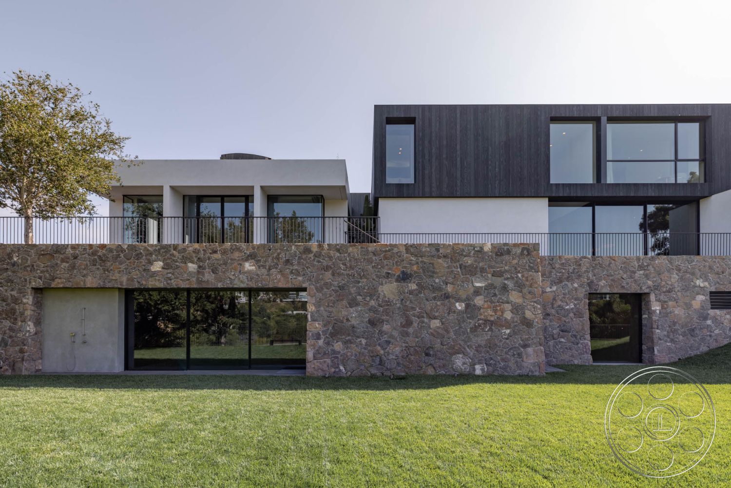 Modern 513 - open floor plan, large glass windows, urban residential setting, two-story house, flat roof design, contemporary architectural style, lush greenery surroundings, modern minimalist architecture, landscaped grass lawn, metal railing balcony, exterior stone facade, natural stone wall cladding, wood paneling siding, exposed concrete base, rectangular balcony design