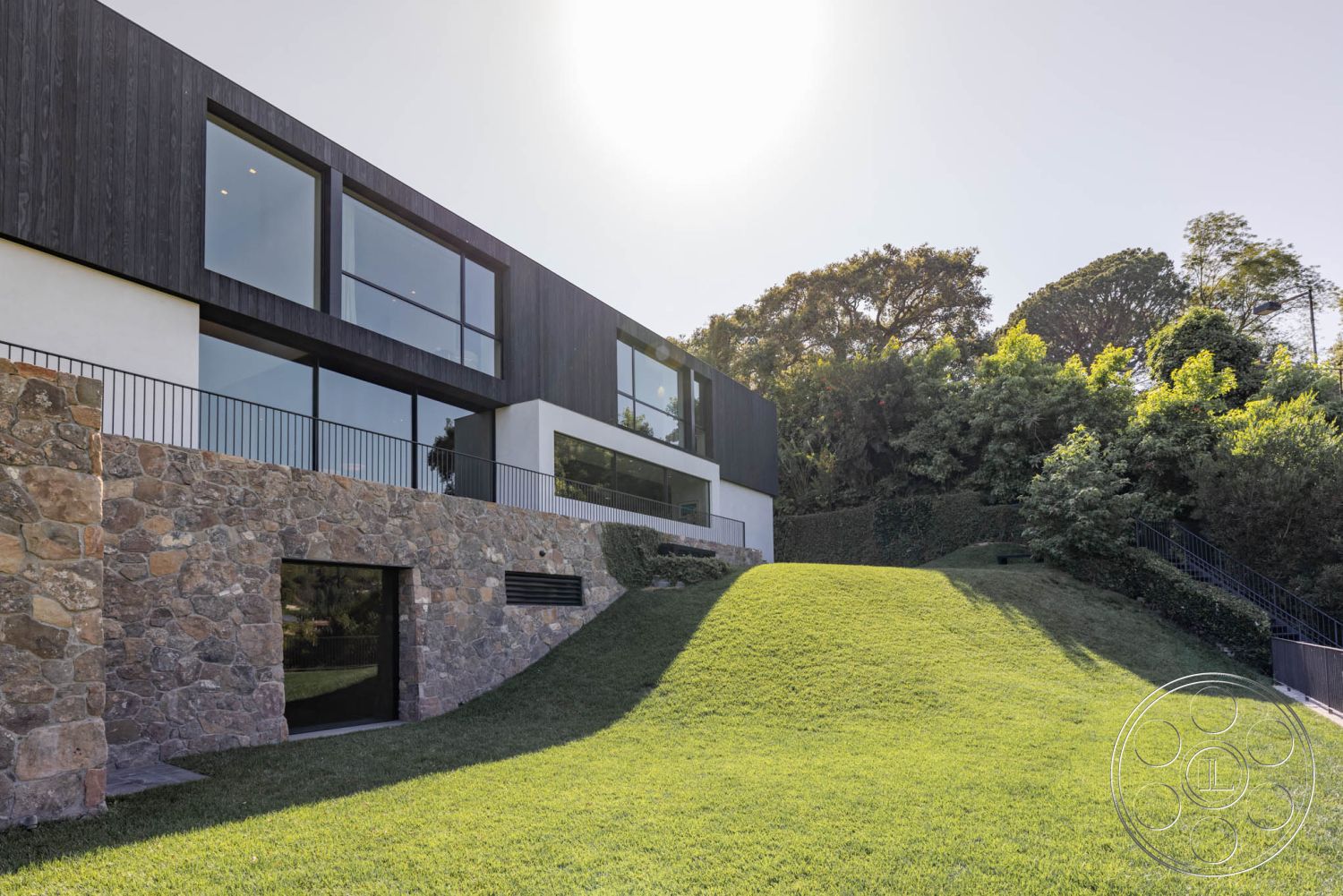 Modern 513 - glass sliding doors, floor-to-ceiling windows, open outdoor space, surrounded by greenery, flat roof design, minimalist architectural style, exterior stone wall cladding, integrated landscaping features, urban modern home, exposed aggregate stone foundation, horizontal wooden siding, modern steel railing, slope grass landscape, natural stone base, hillside residential setting