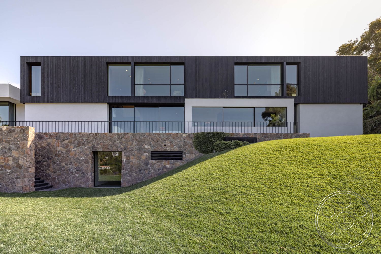 Modern 513 - large floor-to-ceiling windows, integrated landscaping, contemporary architectural style, lush green lawn setting, exterior stone feature wall, minimalist entryway design, geometric building shapes, open terrace with railing, exterior wood plank siding, rounded grass landscape, modern angular design, natural stone steps leading up, smooth concrete foundation wall, hilltop location with a view, metal railings on balcony, horizontal wooden trim accents, modernist facade design