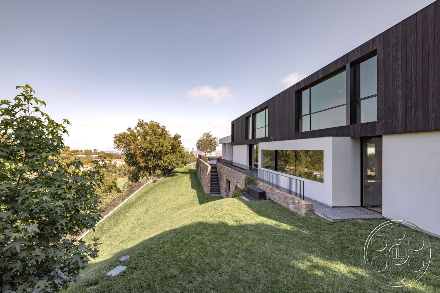 Modern 513 - exterior, large glass sliding door, metal railing, floor-to-ceiling windows, concrete walkway, natural stone steps, stone retaining wall, view of city skyline, open green space, sloped lawn, landscaped garden area, minimalist design details, natural light-filled spaces, wood panel exterior cladding, gabled roofline, urban hillside property, rectangular home layout, modern contemporary architecture, outdoor step terrace