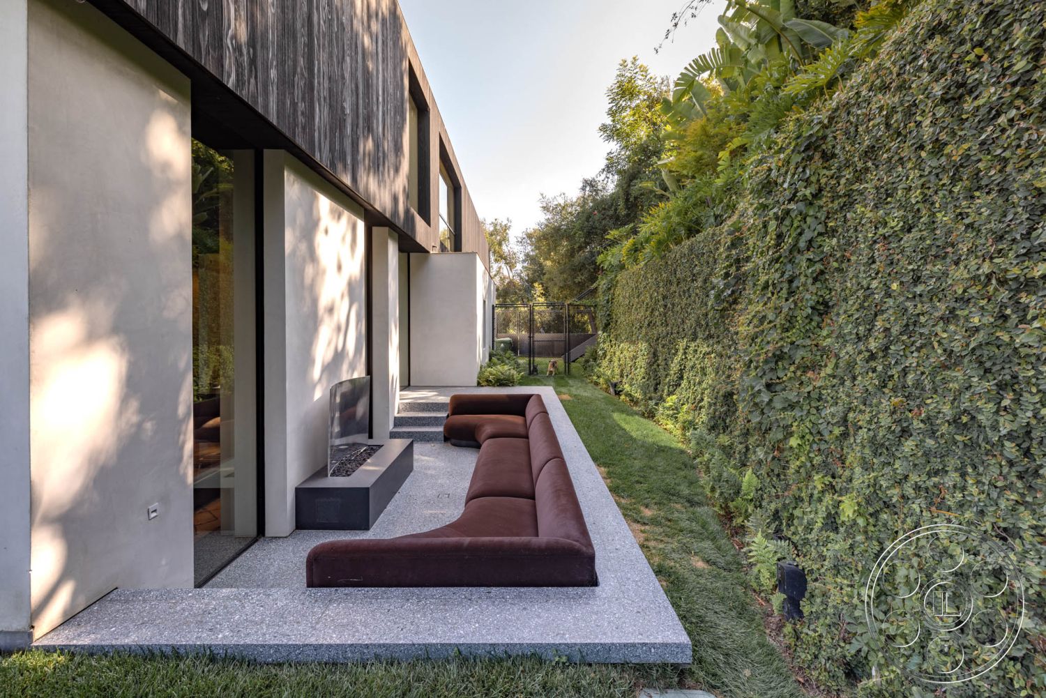 Modern 513 - exterior concrete patio floor, landscaped garden setting, rectangular garden layout, minimalist architectural style, exterior concrete bench seating, modern linear fire feature, brown outdoor upholstery, tall green hedge privacy wall