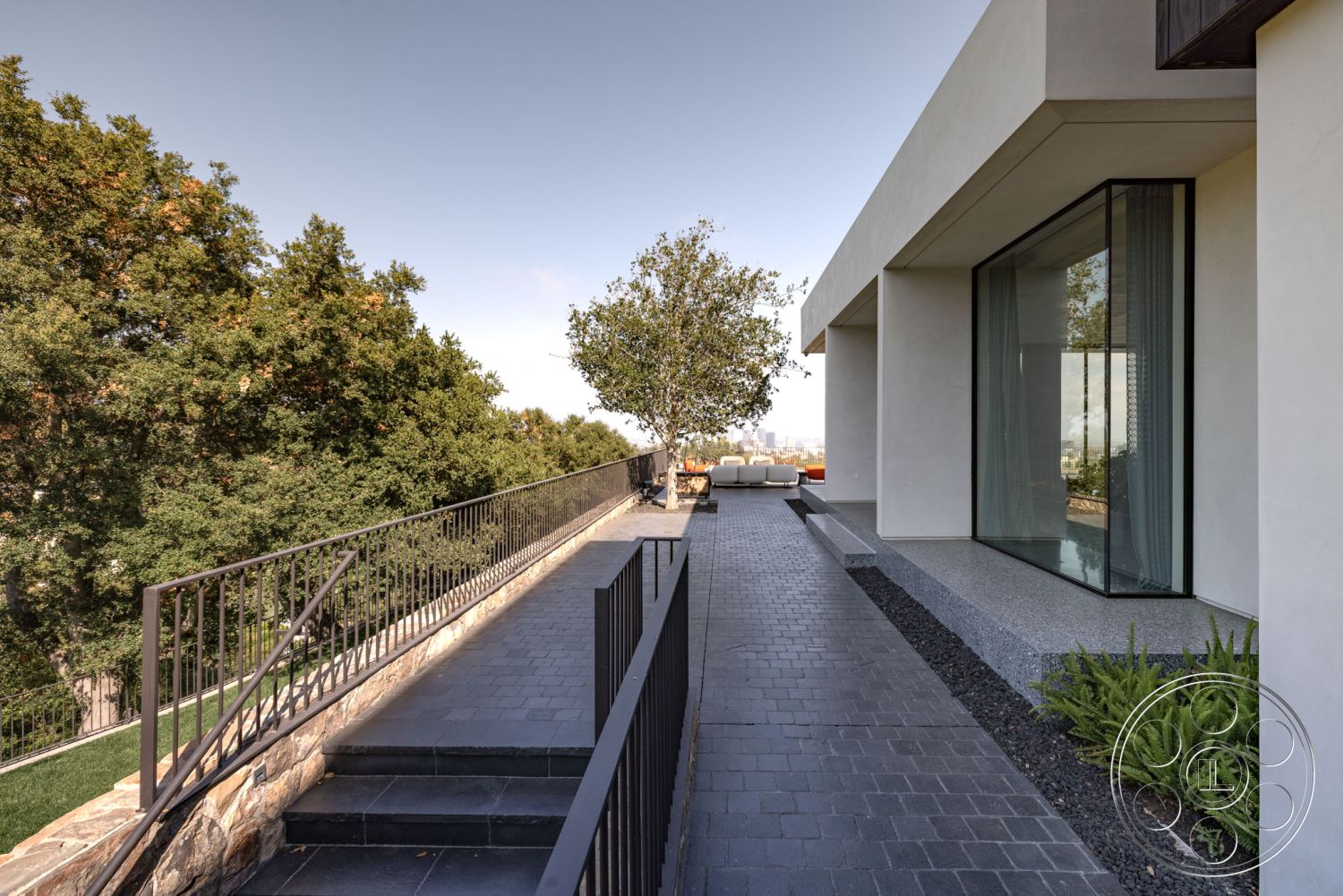 Modern 513 - smooth concrete surface, modern architectural style, urban skyline view, landscaped garden area, concrete patio border, large floor-to-ceiling glass windows, exterior walkway with gravel borders, slate outdoor steps, minimalist concrete walls, metal railing with geometric design, flat-roofed home design, gorgeous tree accentuating space, rectangular pathway layout, natural stone detail in landscaping, outdoor lounge area with modern furniture