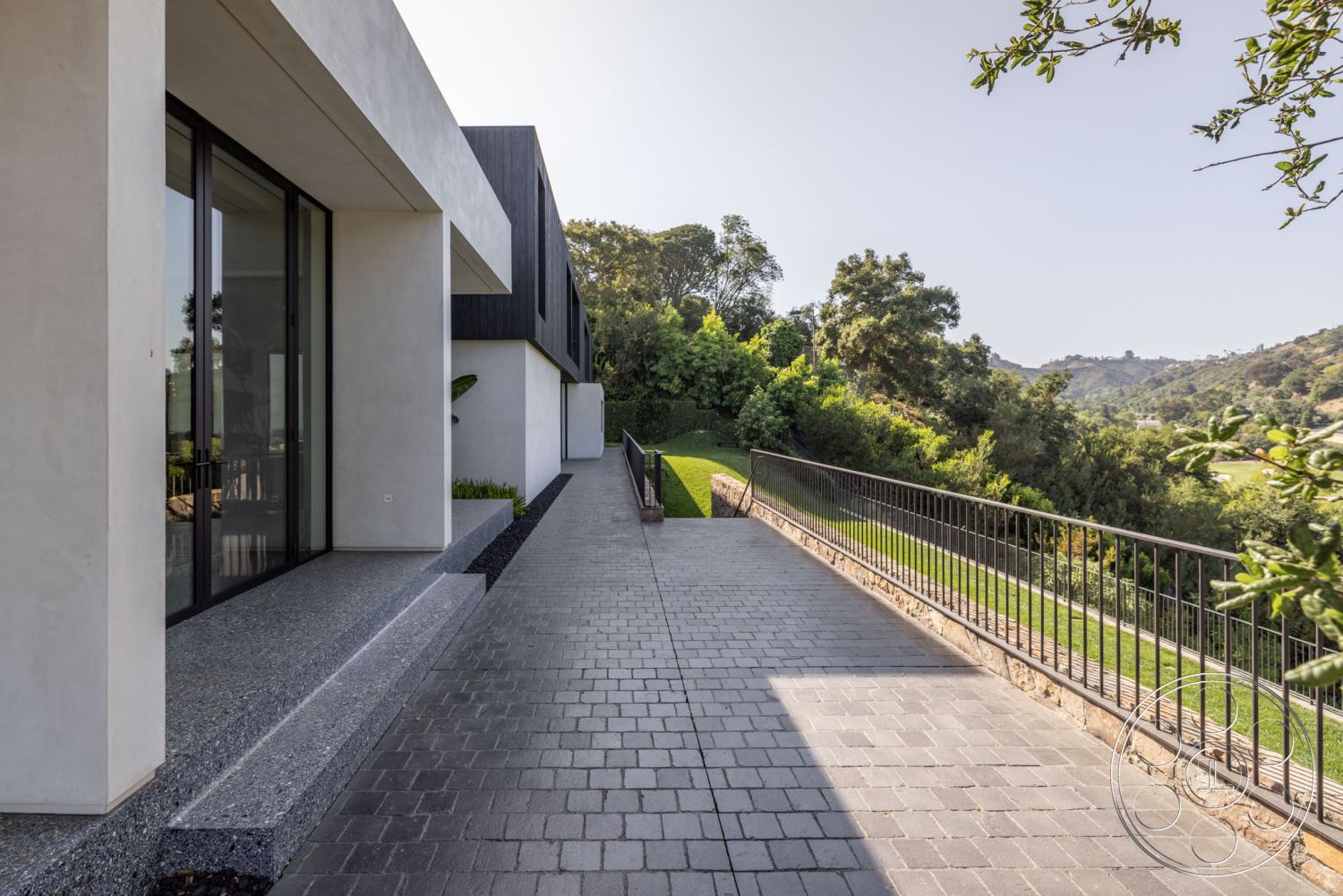 Modern 513 - glass sliding doors, outdoor living space, landscaped garden setting, modern minimalistic design, exterior concrete pathway, natural hillside backdrop, textured concrete step edge, rectangular concrete slab, paver stone driveway, opaque wall panels, low-maintenance garden area, metal railing with vertical balusters, structured landscape elements