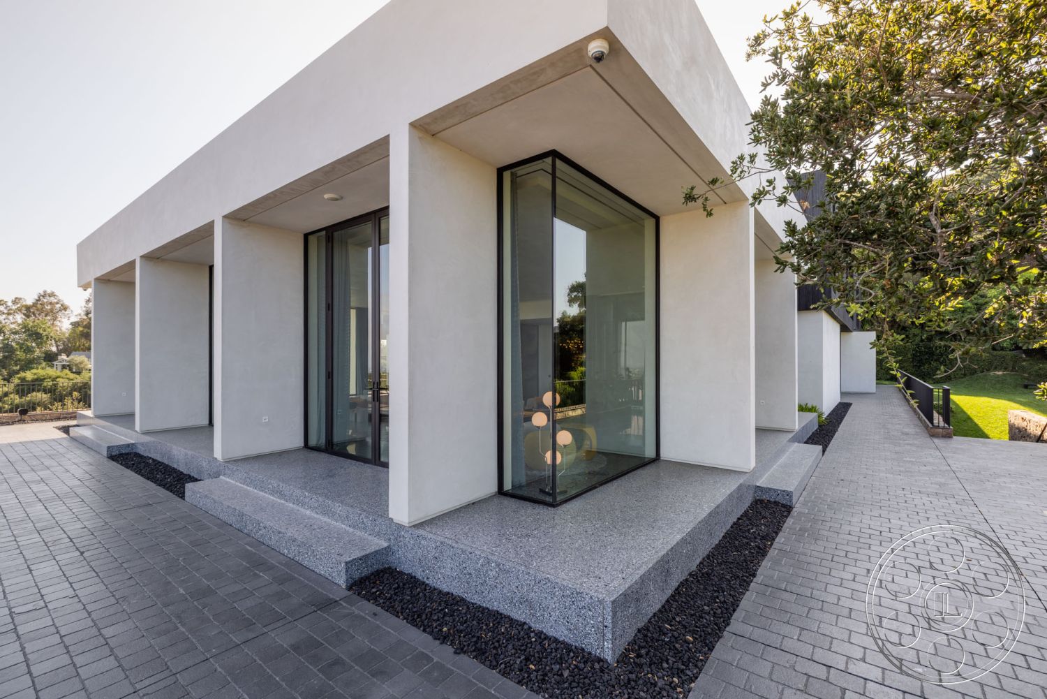 Modern 513 - exterior, clean lines, large glass sliding doors, open floor plan, floor-to-ceiling windows, symmetrical facade, stucco walls, minimalist architecture, rectangular layout, lush greenery backdrop, overhanging eaves, flat roof design, contemporary outdoor living space, textured concrete surfaces, square concrete patio steps, grey granite patio flooring, dark stone landscaping, modern angular shapes, elevated porch, urban context, soft natural light filtering