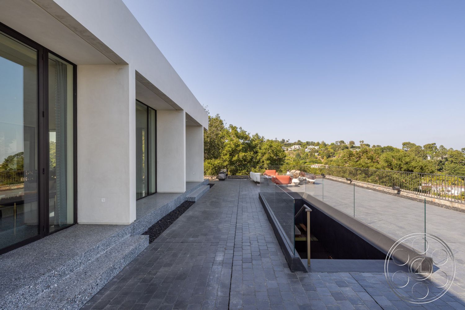 Modern 513 - neutral color palette, concrete pool deck, exterior concrete patio floor, clean lines and geometric forms, floor-to-ceiling glass windows, modern minimalist architecture, integrated lighting features, symmetrical façade, rectangular pool design, granite pool border, exposed aggregate terrace steps, open urban hillside setting, black glass railing details, paved stone outdoor flooring, lounge area with outdoor furniture, lush landscape surrounding property, smooth stucco wall treatment