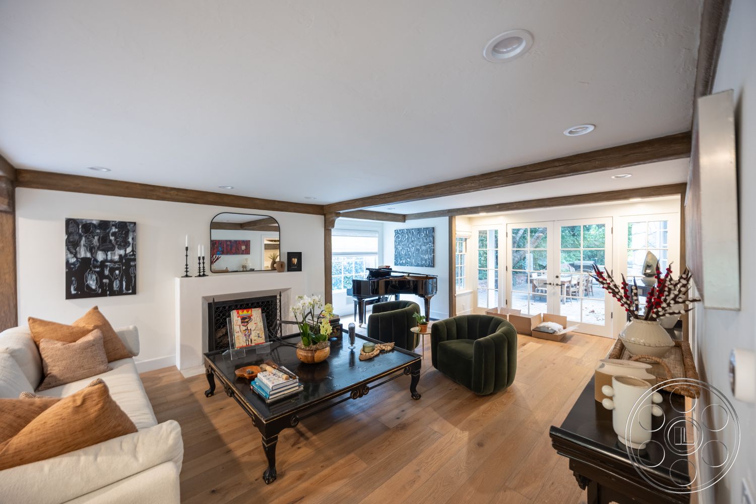 Americana 201 - interior space, decorative wall art, light-filled environment, welcoming atmosphere, open-concept design, exposed wood ceiling beams, hardwood living room floors, white painted walls, stone fireplace surround, floor-to-ceiling glass doors, cozy living area, modern black coffee table, plush velvet armchairs, curtained windows with garden view, plant decoration in vase, vintage-style mirror, neutral-colored sectional sofa, candle holders on fireplace, modern piano in corner