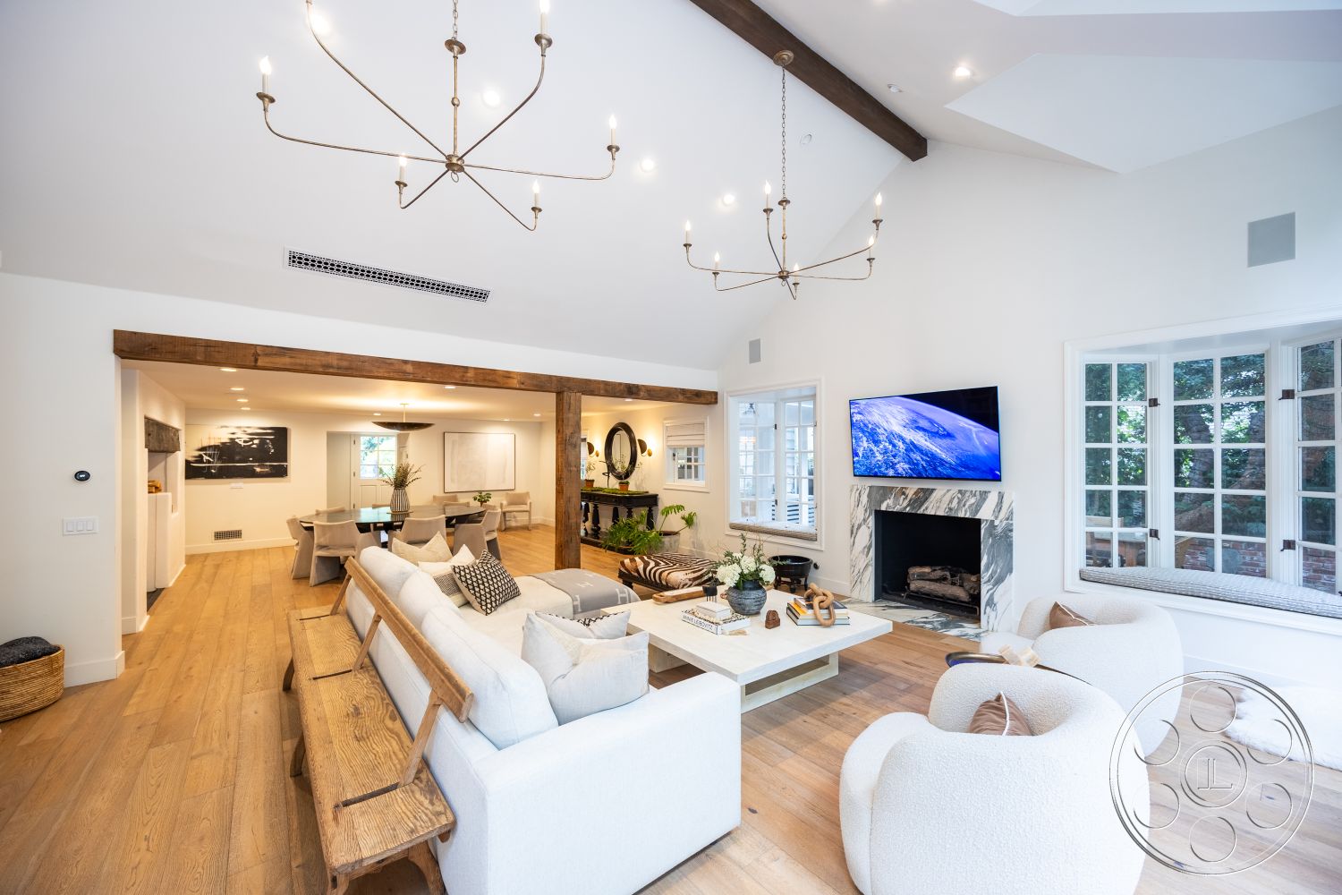 Americana 201 - interior minimalist decor, interior hardwood living room floors, interior white painted walls, interior natural light-filled space, interior contemporary design elements, interior cozy seating area, interior modern chandelier lighting, interior open-concept living space, interior marble fireplace surround, interior warm color palette, interior large bay windows, interior built-in shelving units, interior vaulted living room ceiling with exposed wood beams, interior circular dining table, interior textured throw pillows