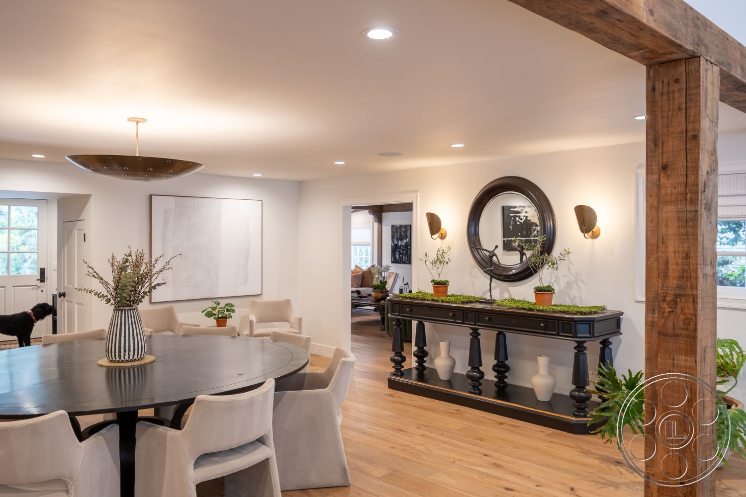 Americana 201 - neutral color palette, hardwood flooring, modern lighting fixtures, upholstered dining chairs, inviting entryway, casual dining area, round dining table, contemporary art on walls, welcoming ambiance, natural light from windows, textured wall treatment, exposed wood ceiling beams, smooth wall finish, crown molding details, spacious open floor plan, houseplants in decorative pots, black console table with decorative vases, large wall-mounted mirror, stylish wall sconces