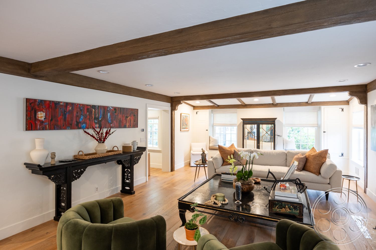 Americana 201 - inviting atmosphere, open floor plan, exposed wood ceiling beams, interior living space, modern interior design, textured plaster wall finish, hardwood flooring in living room, white painted walls, natural light from multiple windows, cozy living area, soft ambient lighting fixtures, decorative black console table, upholstered green accent chairs, neutral fabric sofa with throw pillows, large window with white trim, glass and wood coffee table, artwork featuring vibrant colors, decorative plant arrangement, classic home architecture style