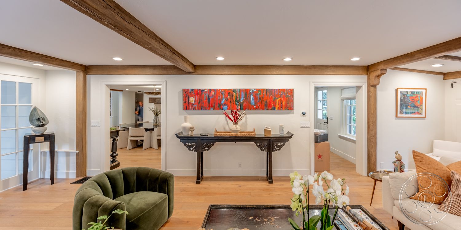 Americana 201 - artwork on wall, natural light from windows, open-concept layout, decorative floral arrangements, exposed wood ceiling beams, hardwood living room floors, contemporary furniture design, white painted walls, cozy living room ambiance, modern art decoration, glass partitioning in interior, black console table, green velvet accent chair, neutral colored sofa, suburban interior