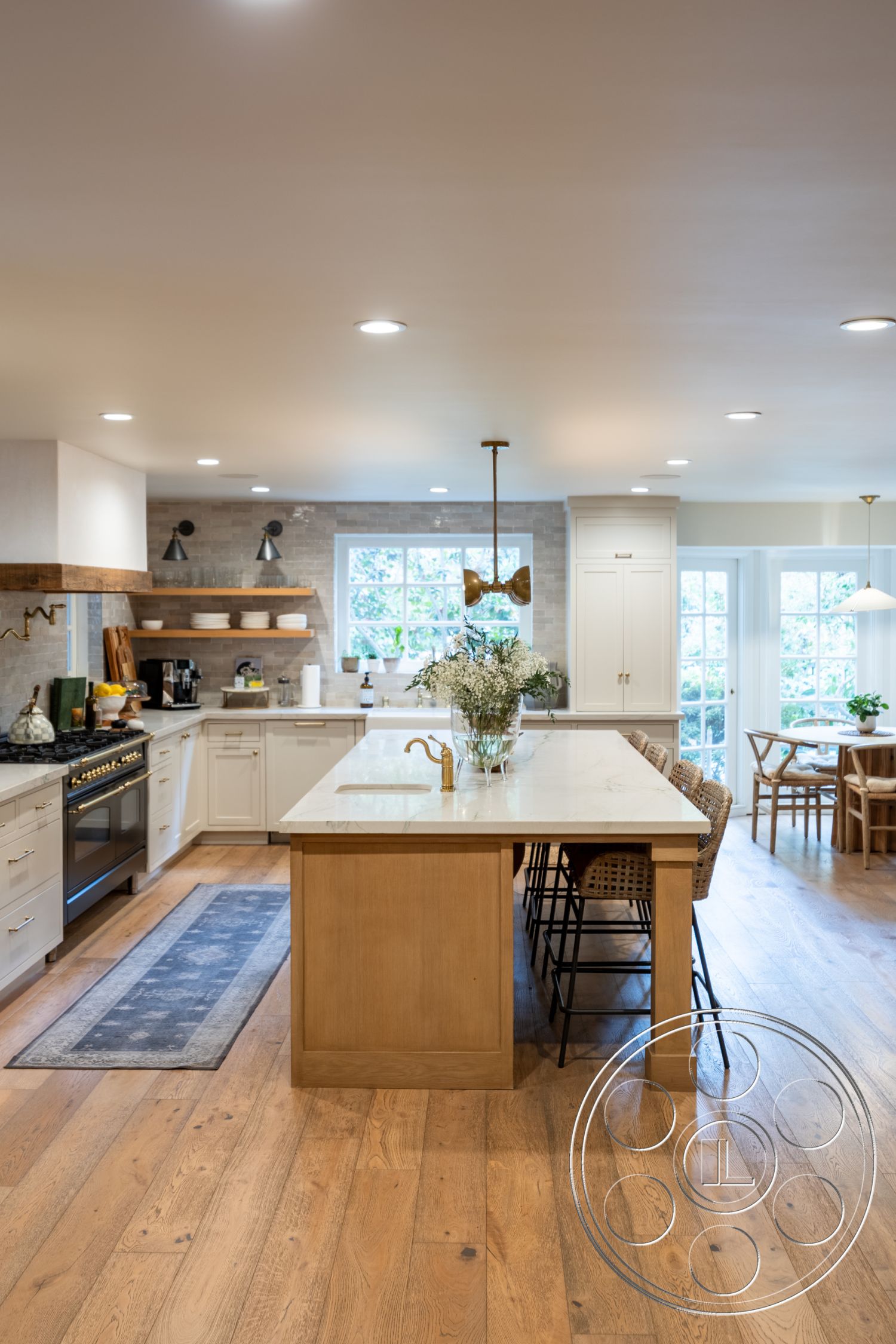 Americana 201 - neutral color palette, natural light, open floor plan, stainless steel appliances, textured plaster walls, interior kitchen, hardwood kitchen flooring, exposed wood beam ceiling, large casement windows, white shaker kitchen cabinets, pendant lighting over kitchen island, marble countertop kitchen island, brass kitchen faucet, subway tile kitchen backsplash, farmhouse-style dining nook