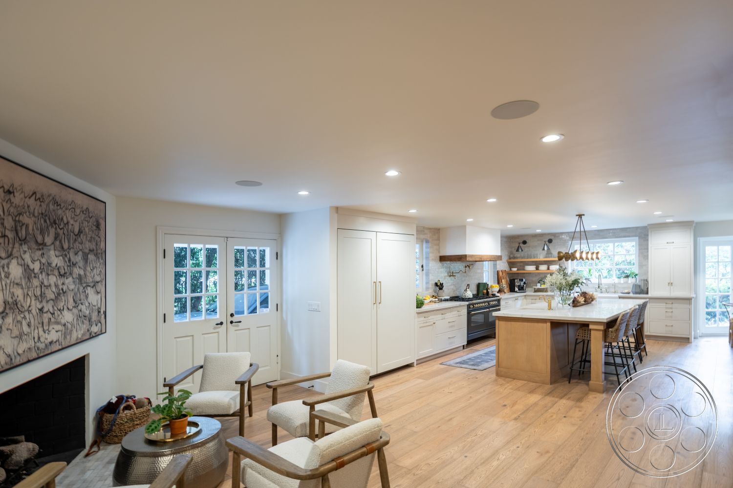 Americana 201 - textured area rug, modern rustic decor, natural greenery view, open concept living space, soft natural lighting, double French doors, glass pendant lighting, black stainless steel appliances, light-filled space, exposed wood ceiling beams, marble kitchen island countertop, hardwood kitchen flooring, white shaker kitchen cabinets, subway tile kitchen backsplash, farmhouse dining chairs, fireplace with black brick surround, seamless flow between kitchen and living area, interior residential kitchen