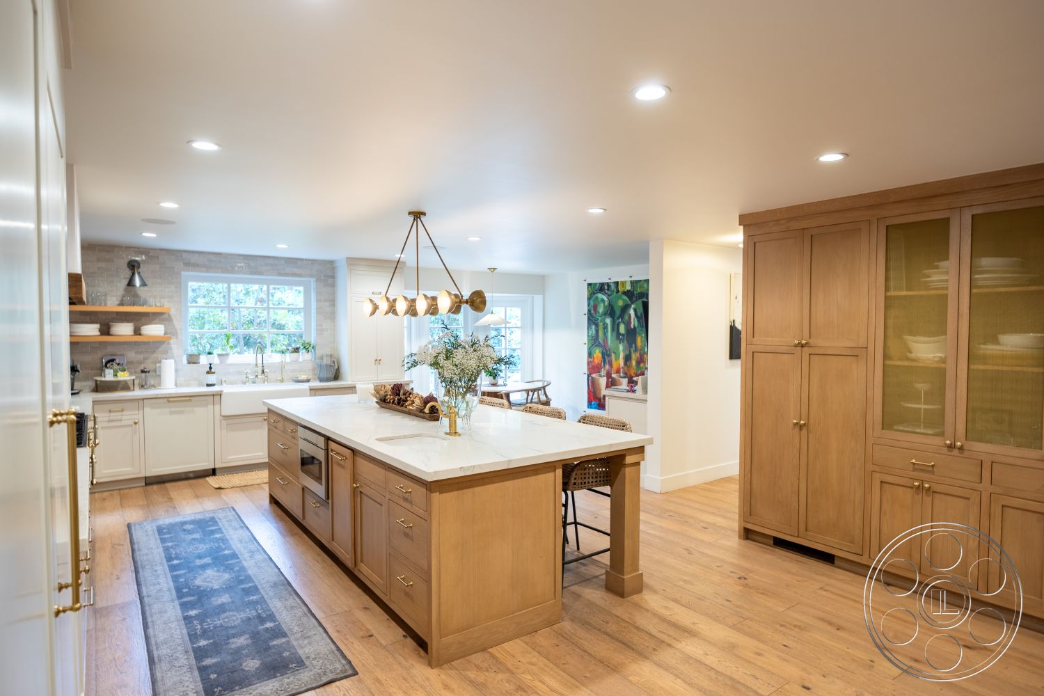 Americana 201 - stainless steel appliances, open concept layout, modern pendant lighting, natural light from large windows, interior kitchen, marble kitchen island countertop, hardwood kitchen floors, white painted walls, exposed brick accent wall, wooden cabinetry with glass doors, double basin stainless steel sink, decorative kitchen rug, rustic wood shelving, chair seating at kitchen island, home design with contemporary touches